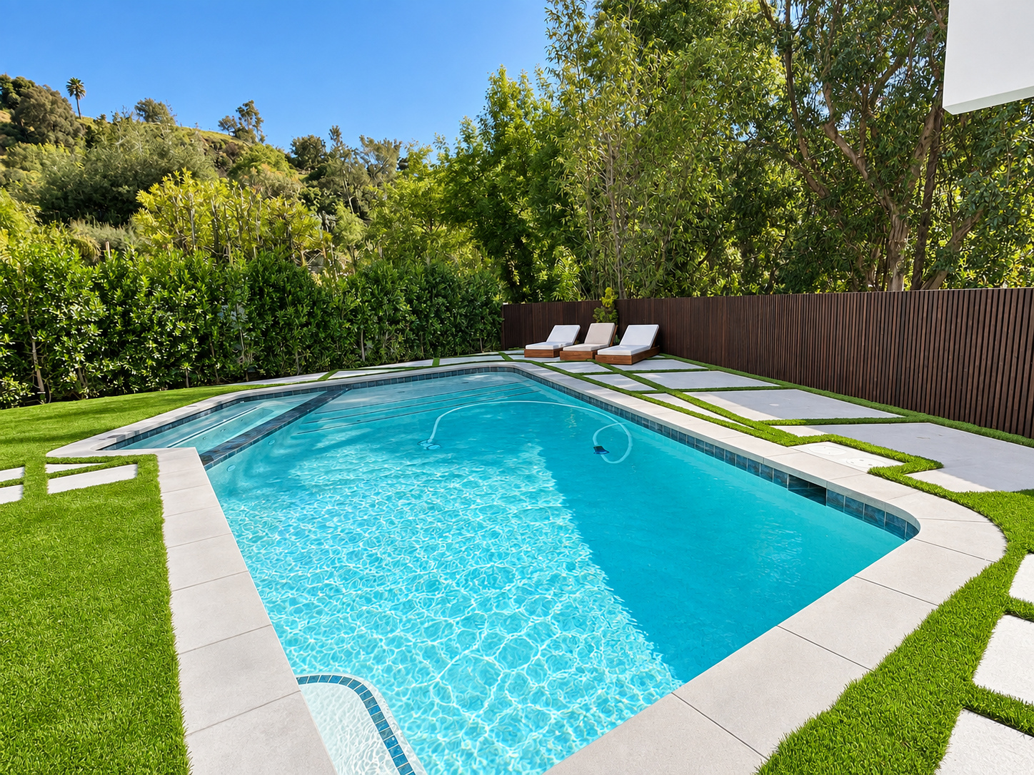 Completed backyard remodel with a pool, artificial turf and large-format concrete pads by Green Design and Build