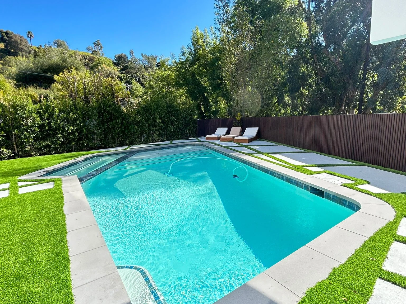 Completed backyard remodel with a pool, artificial turf and large-format concrete pads by Green Design and Build