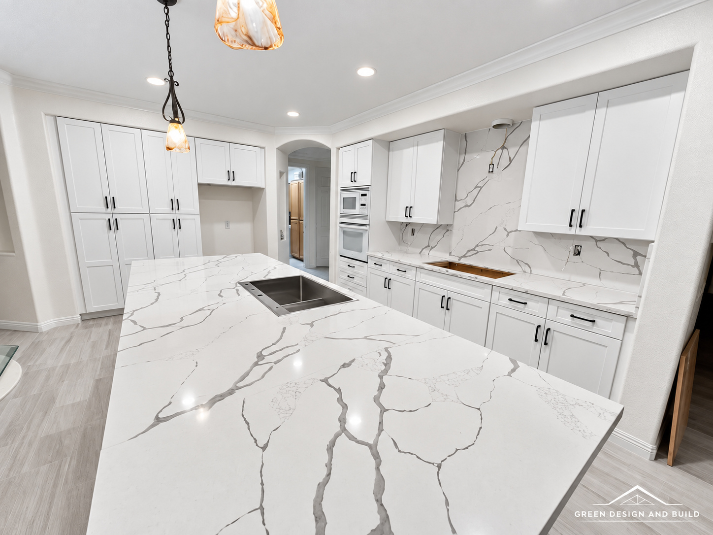 Second kitchen area in the same Burbank home with a quartz island and sink, full-height quartz slab backsplash and wall oven, photographed before the cooktop was installed
