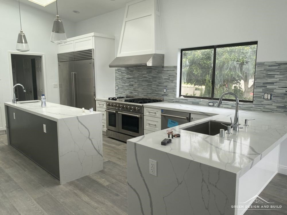 Kitchen with a white quartz waterfall island, plaster hood and professional range in a Burbank home