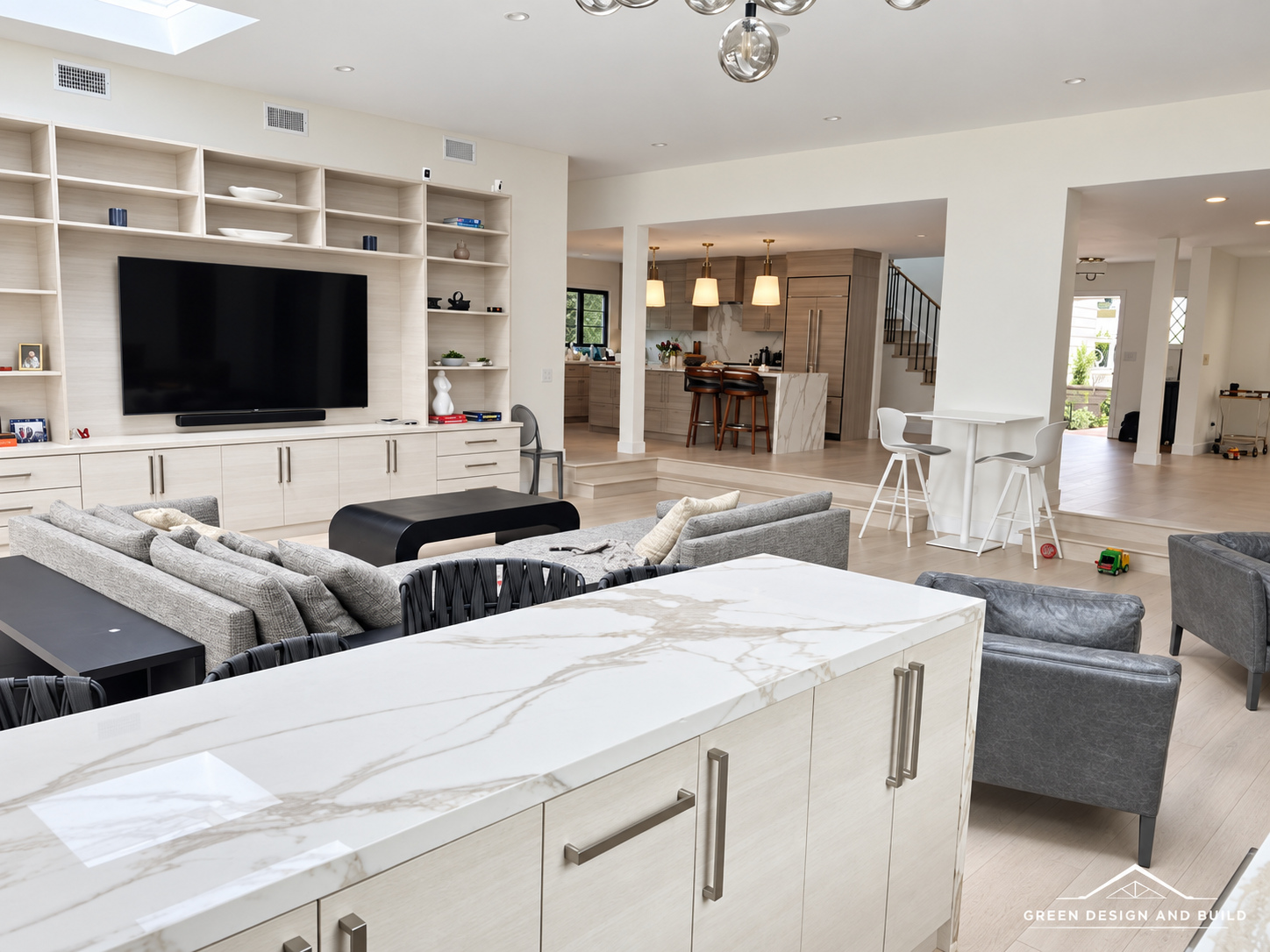 Living room of the same Burbank home with a built-in media wall, sectional sofa and the family kitchen beyond