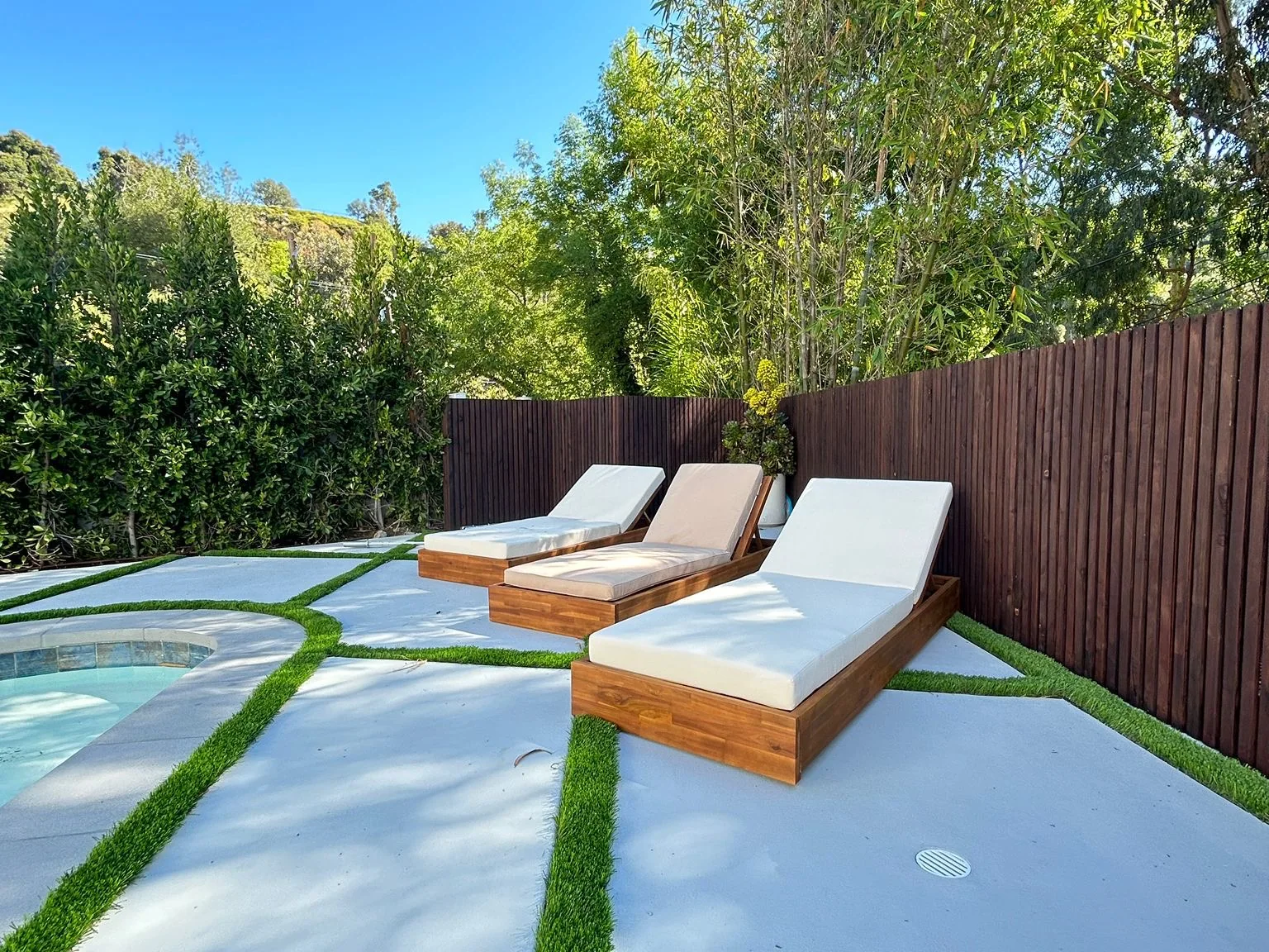 Poolside patio of large concrete pads set with turf joints, with timber loungers