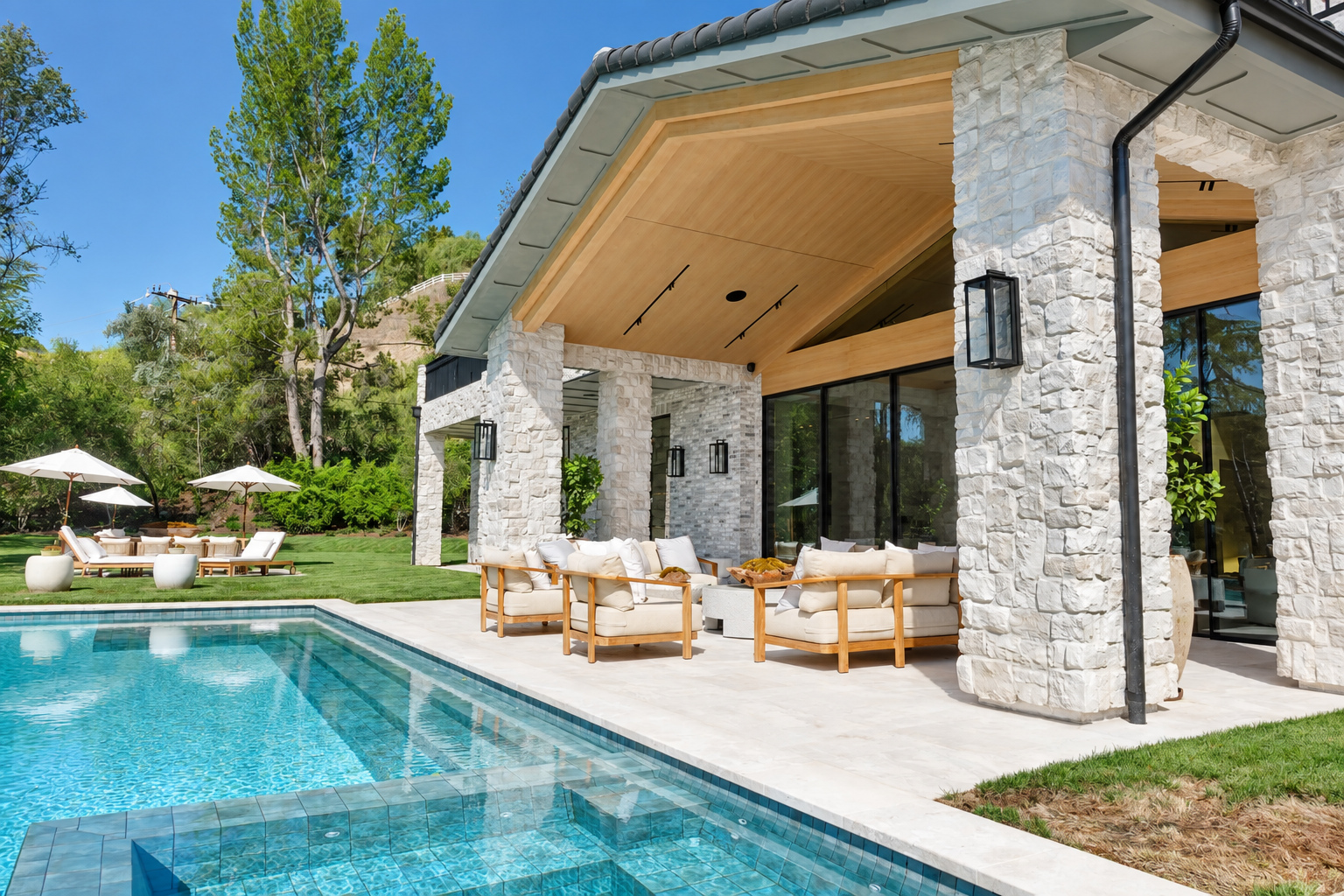 Solid patio cover with stone columns, a wood-lined vaulted ceiling and clay tile roof beside a pool in Hidden Hills