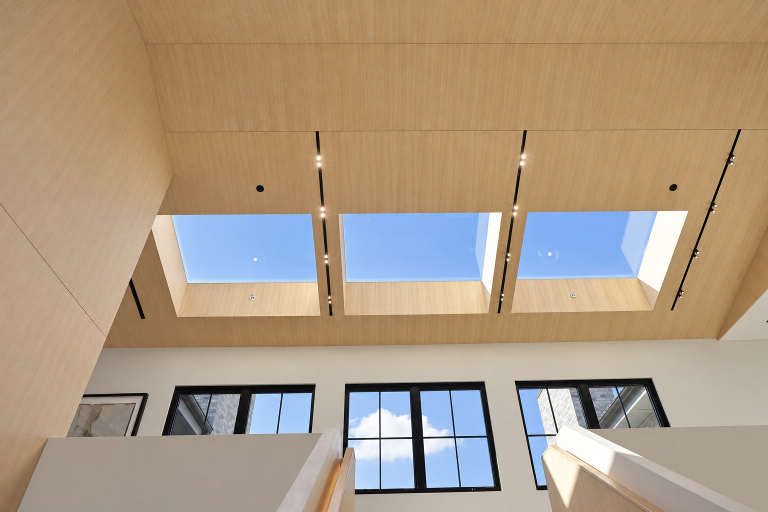 Double-height living space with three skylights in a white oak ceiling above a two-storey black steel window wall