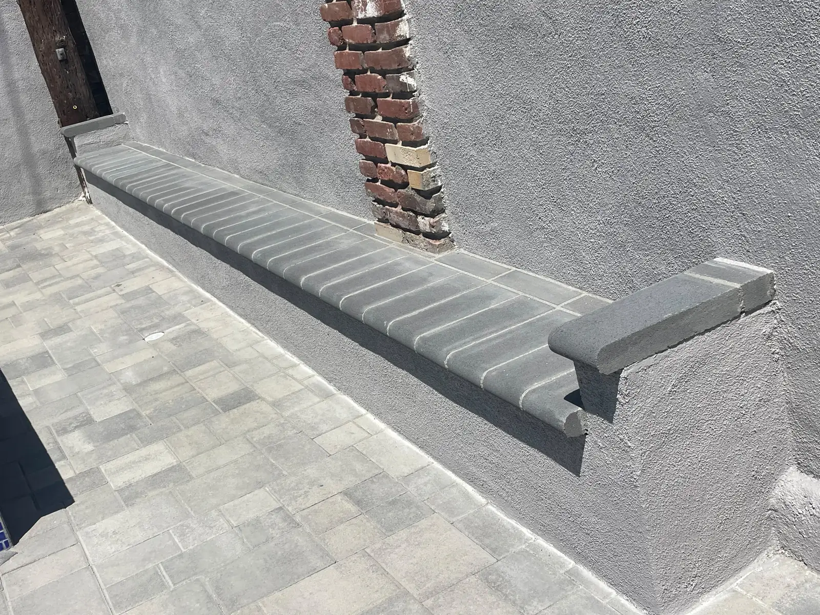 Grey stucco perimeter wall with a red-brick pilaster beside the built-in paver bench