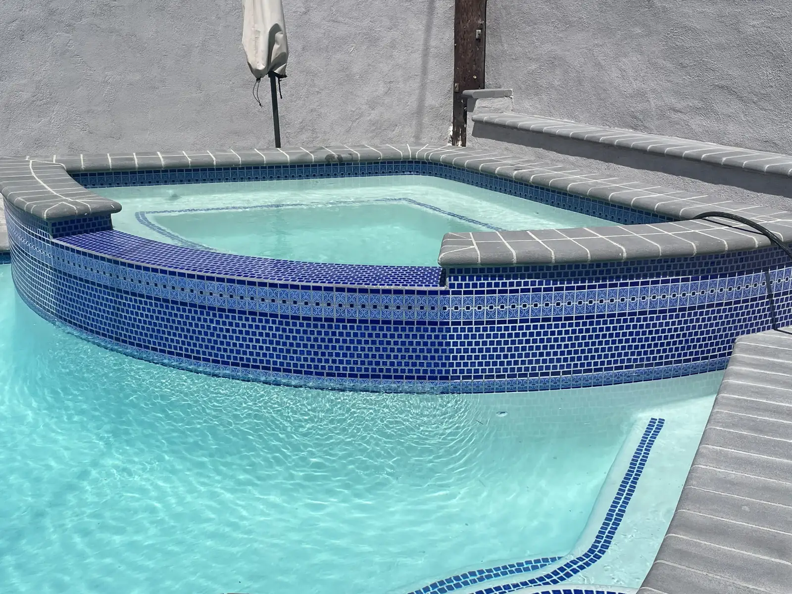 Blue glass mosaic tile and decorative border band on the raised spa wall, with grey bullnose coping