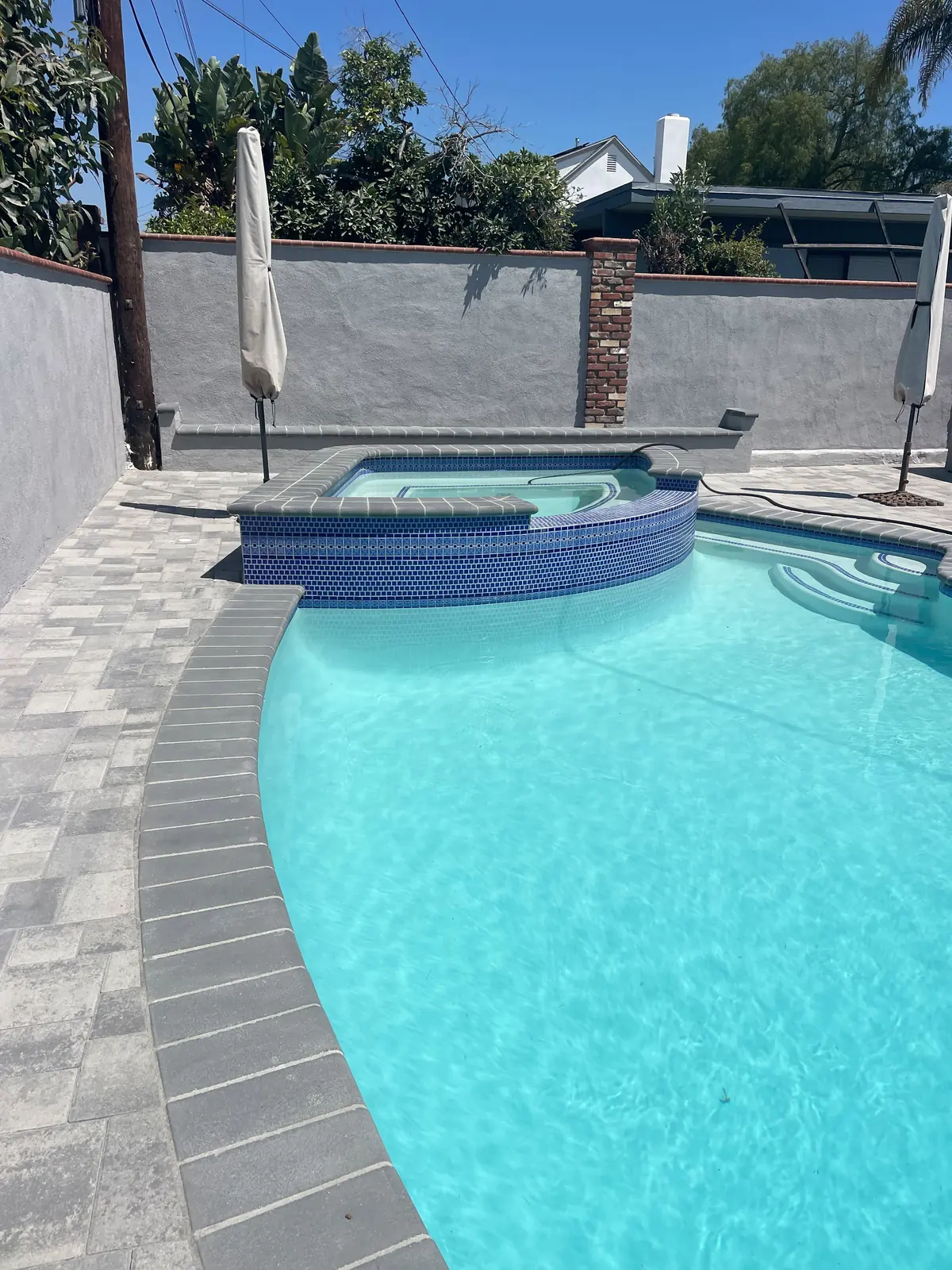 Raised spa spilling into the pool, with the shade umbrella and paver deck