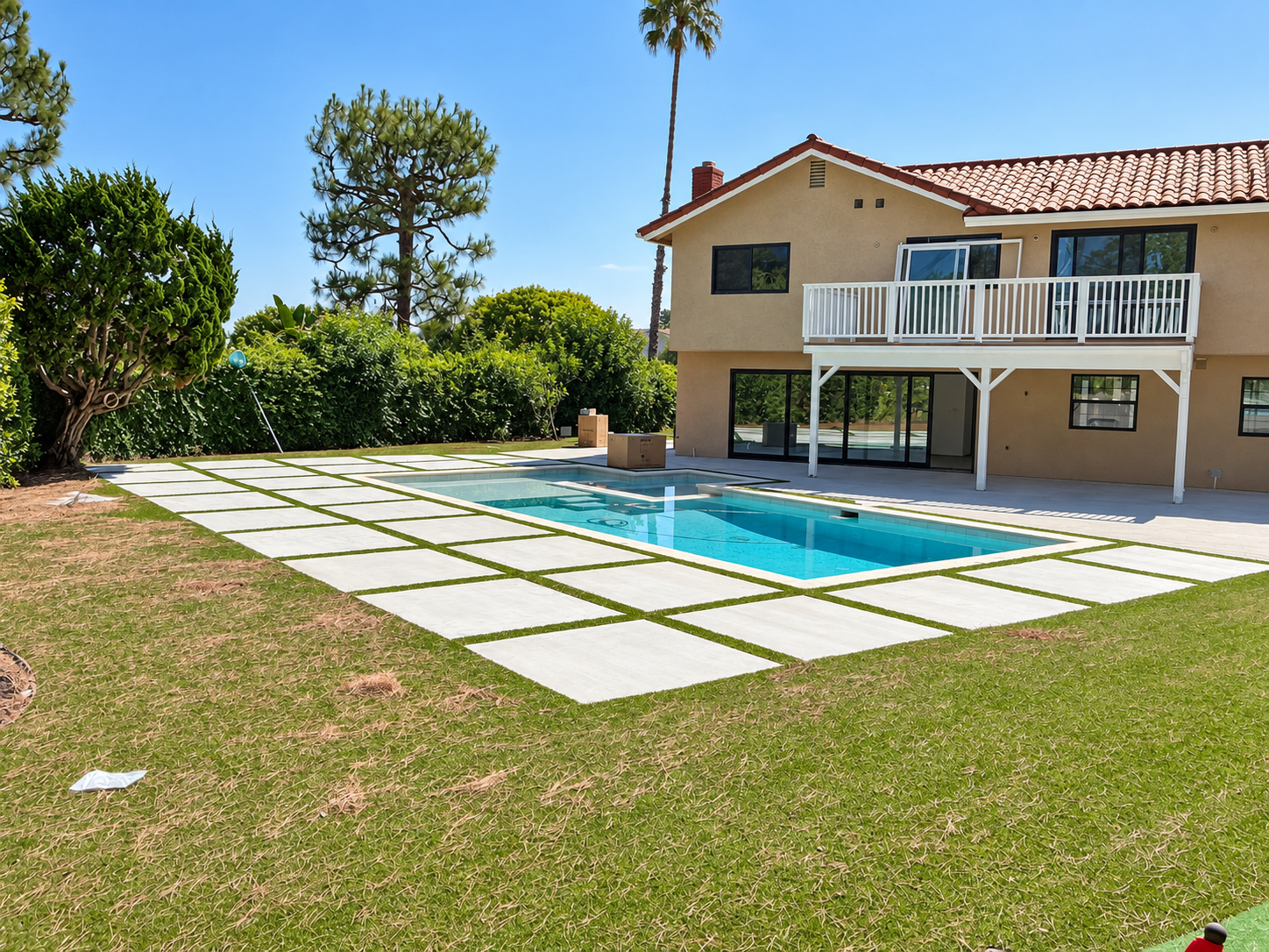 Backyard remodel with a rebuilt pool, large-format pavers set in artificial turf and a two-story house with a balcony