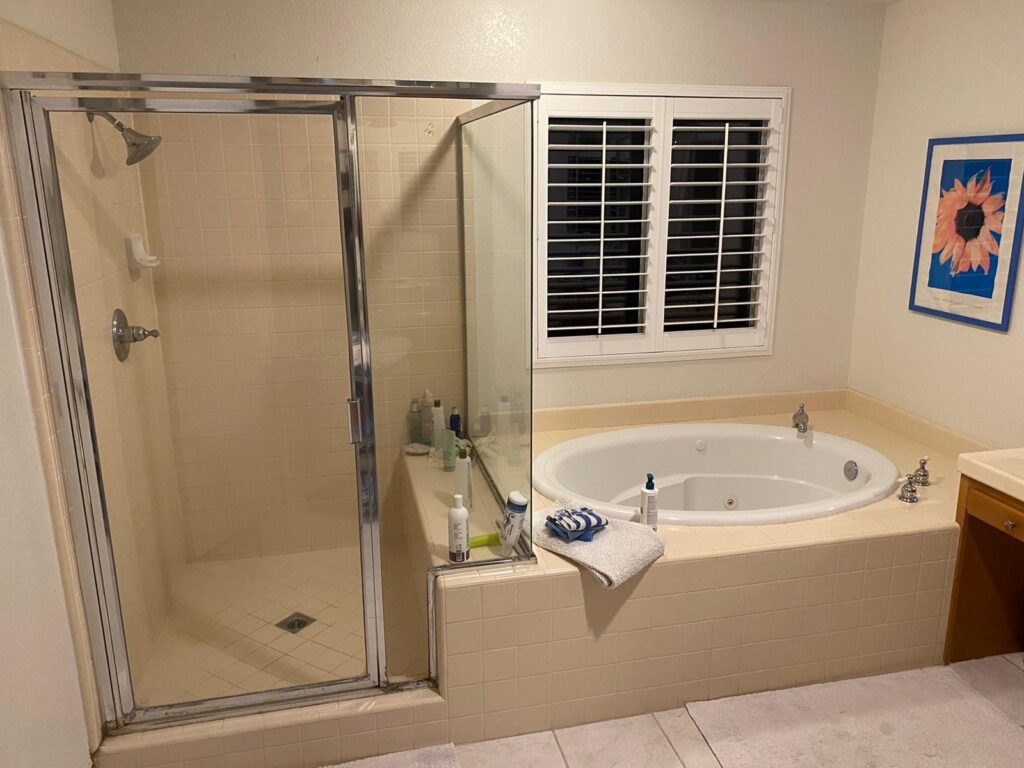 Corner soaking tub on a platform beside a framed glass shower before remodelling, Irvine bathroom