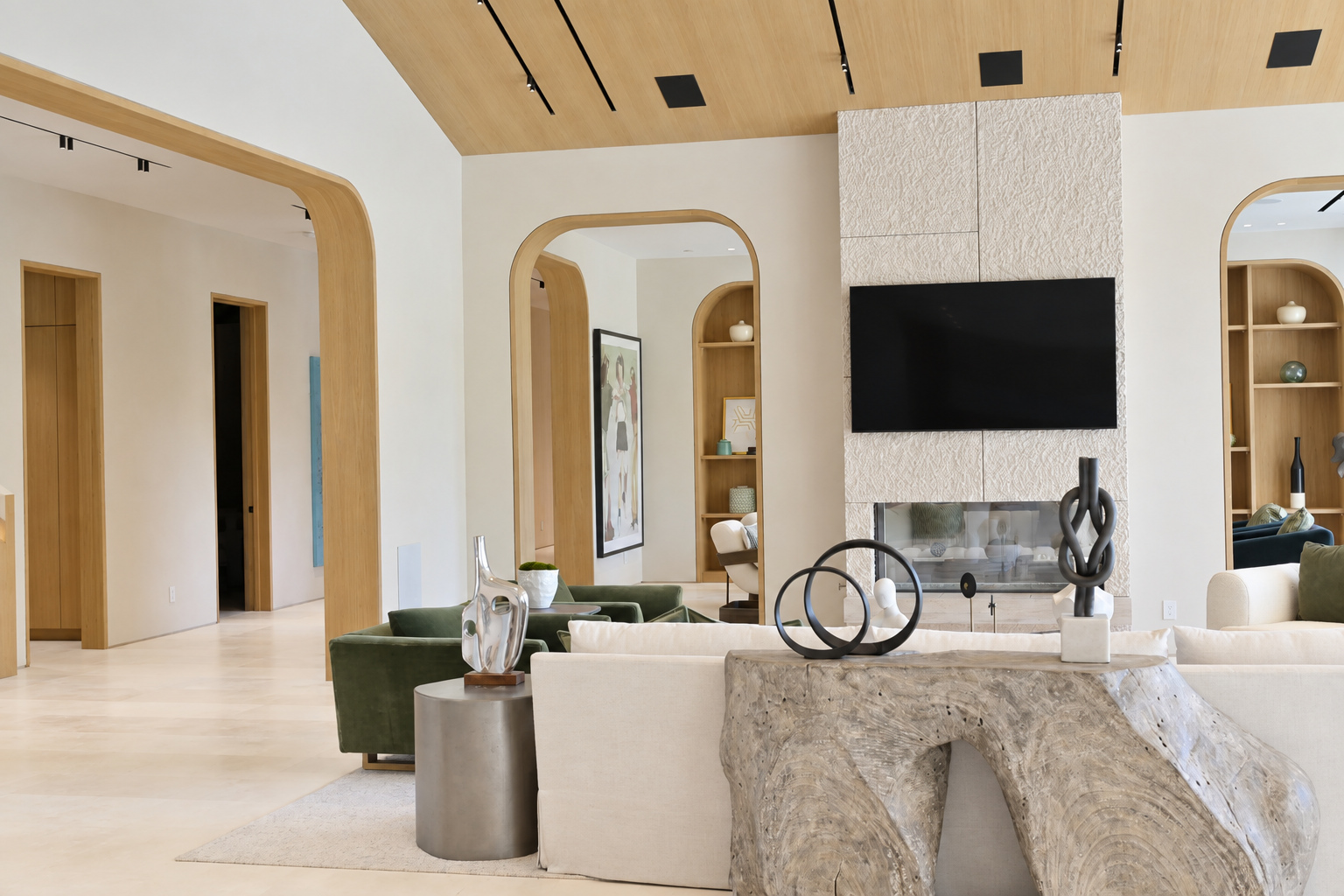 Great room with a vaulted white oak ceiling, arched openings and a see-through fireplace in a textured limestone surround