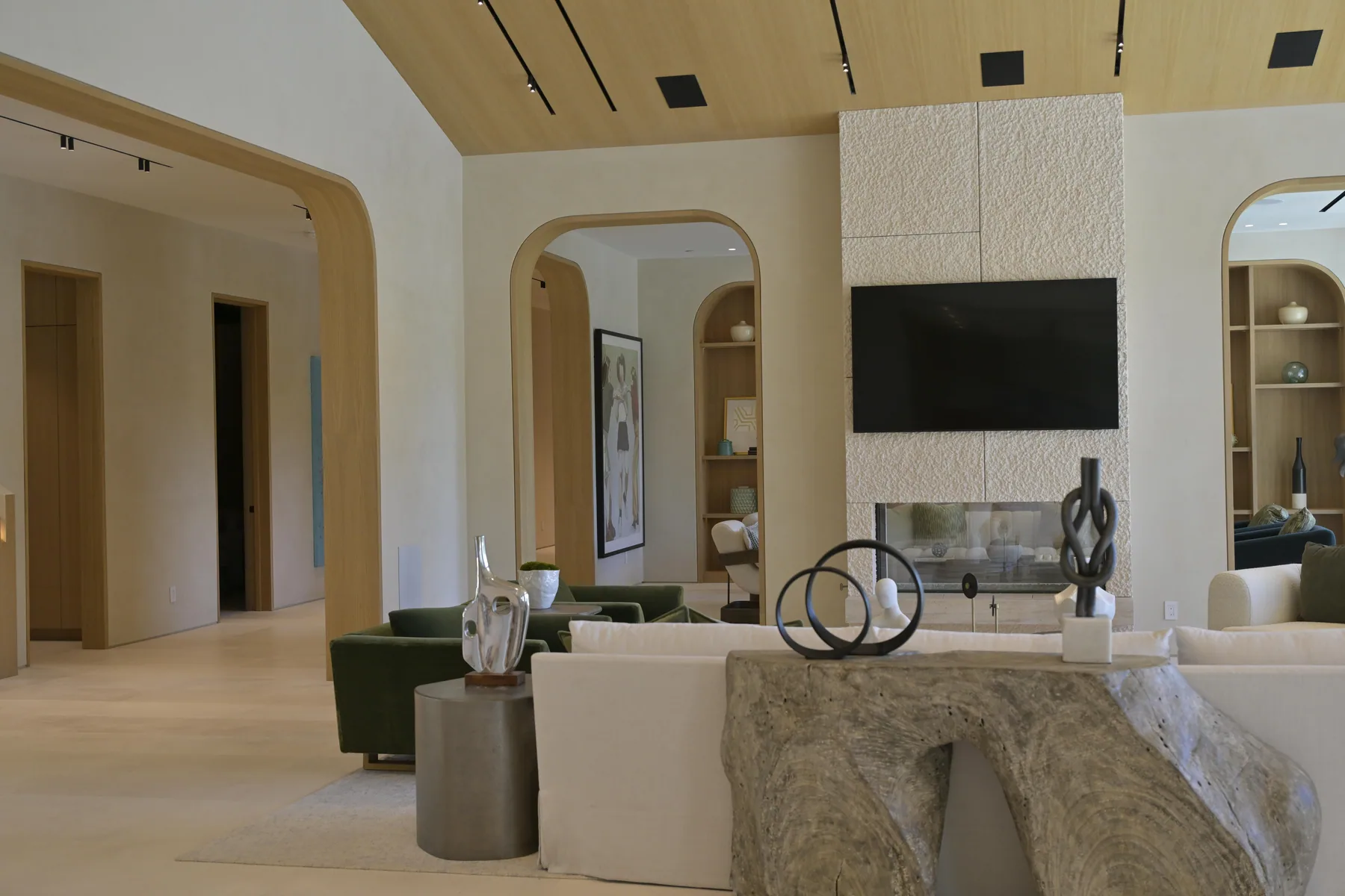 Great room with a vaulted white oak ceiling, arched openings and a see-through fireplace in a textured limestone surround