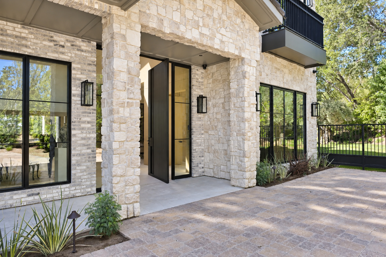 Stone entry loggia with a black steel pivot door opening onto a paver motor court at a Hidden Hills home
