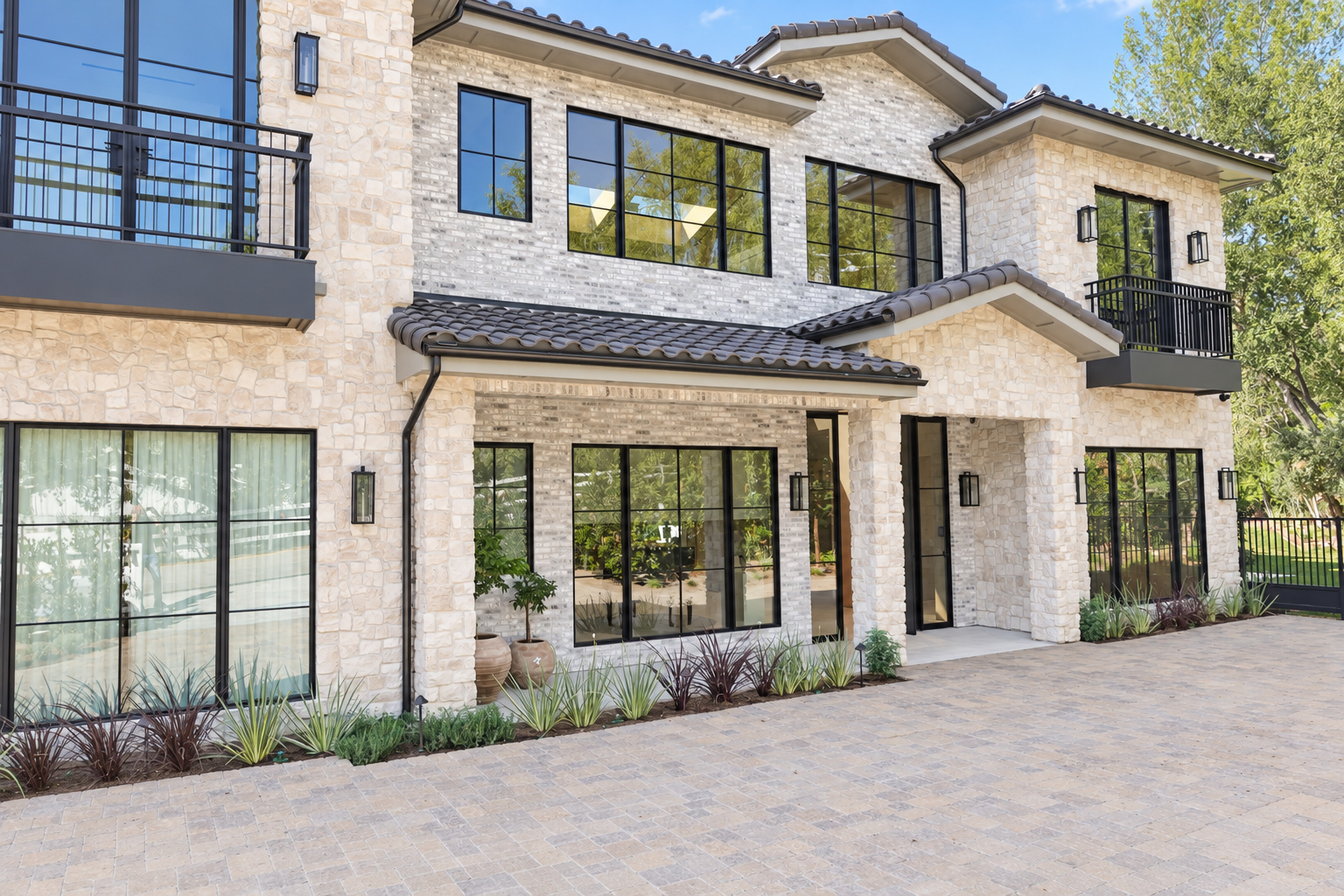 Two-story stone veneer home with clay tile roof, steel windows and a paver motor court, built by Green Design and Build