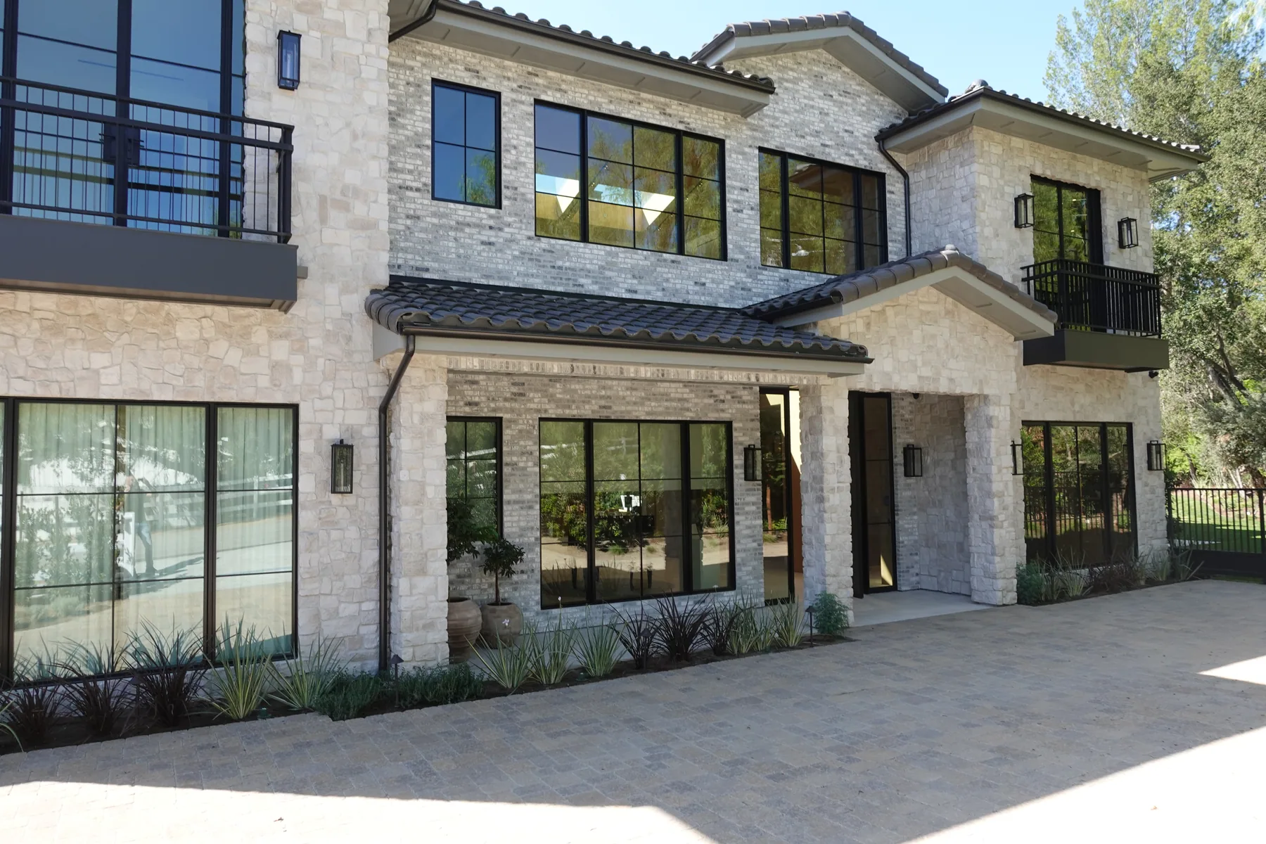Two-storey stone veneer home with clay tile roof, steel windows and a paver motor court, built by Green Design and Build