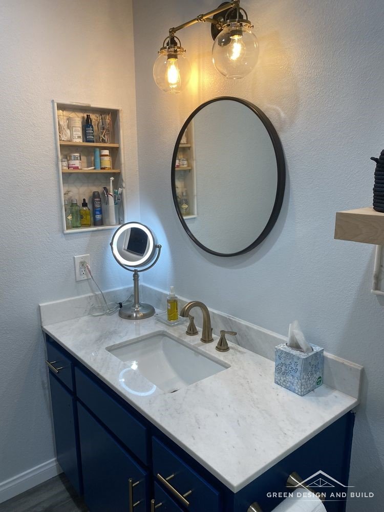 Round black mirror flanked by Edison bulb sconces above a navy vanity in West Hollywood