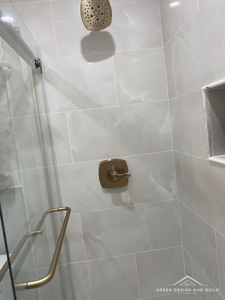 Grey tiled shower with brass fittings behind sliding glass in a West Hollywood bathroom
