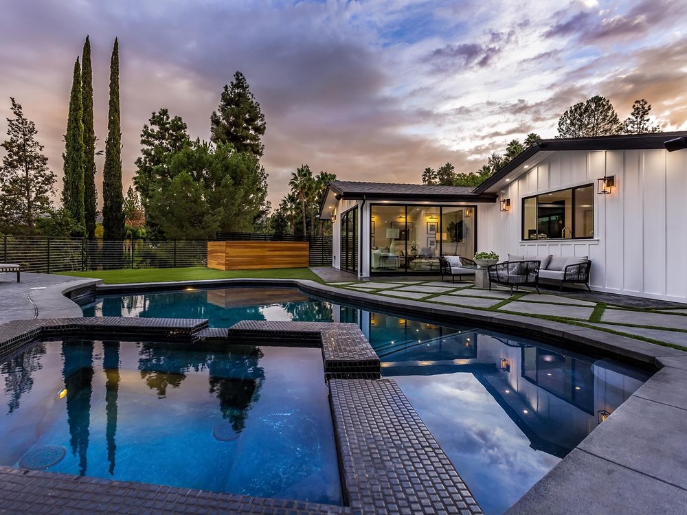 Rebuilt swimming pool, raised spa and paved terrace behind a Woodland Hills home at dusk