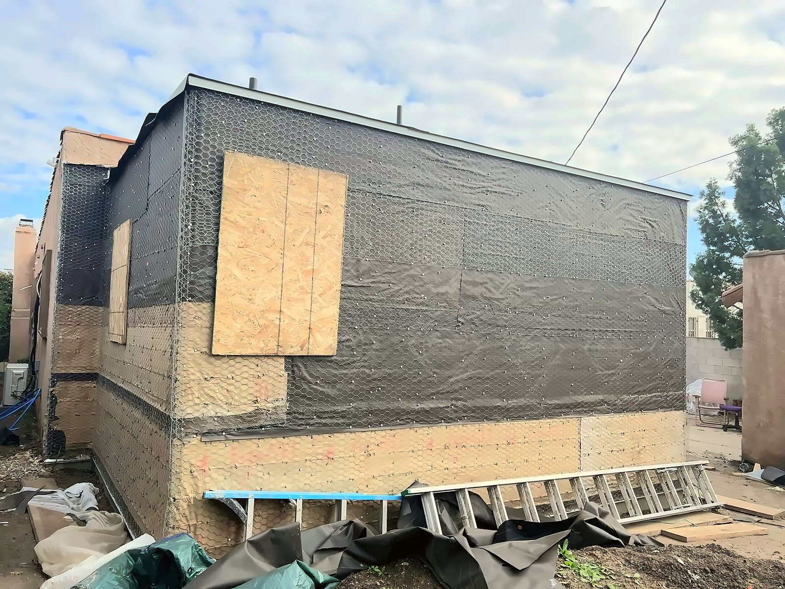 Wood-frame wall covered in black building paper and wire stucco lath before the first plaster coat