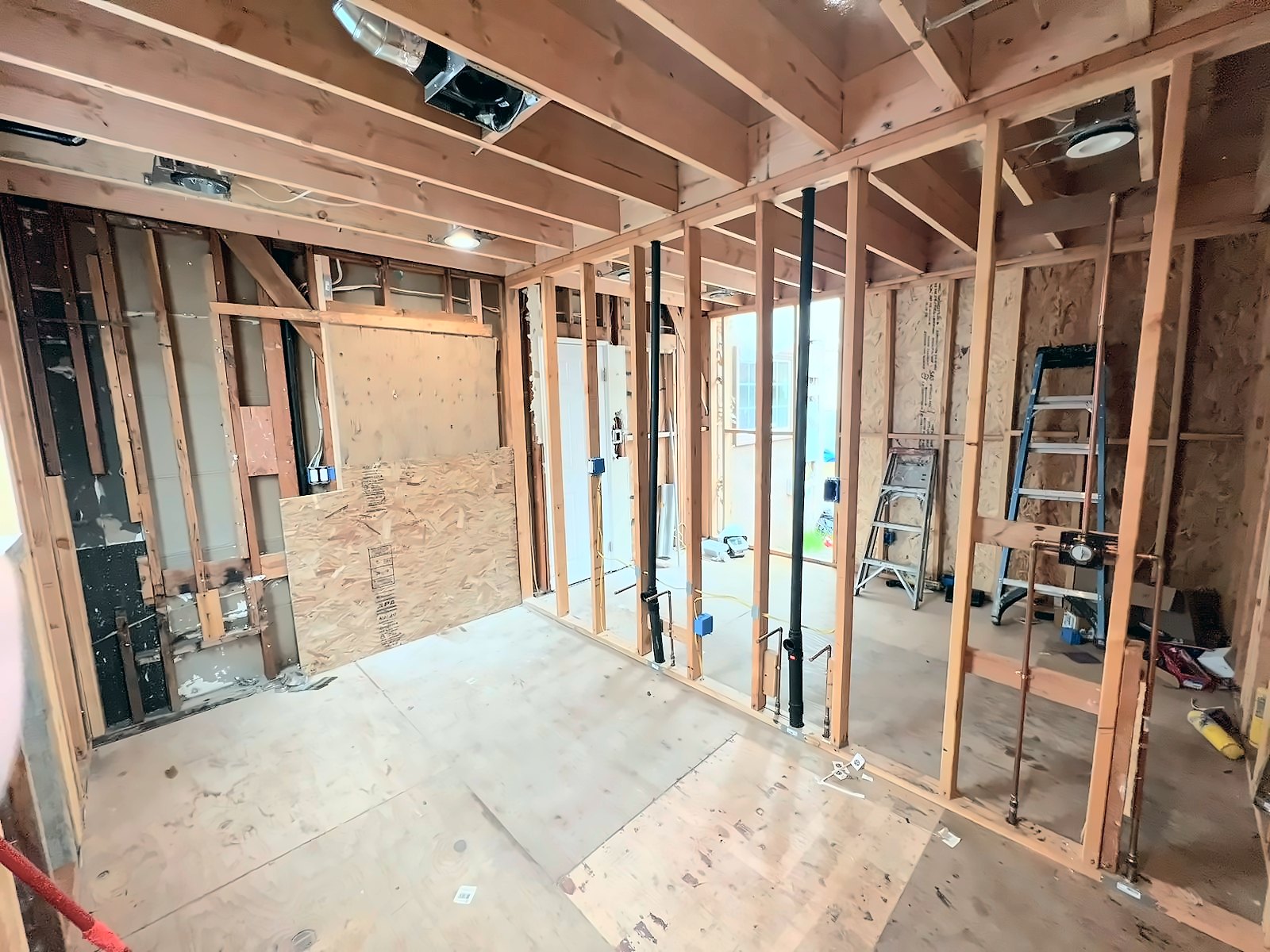 Open stud walls during an attached ADU build in Los Angeles, with red PEX water lines and black ABS drain pipe roughed in before insulation and drywall
