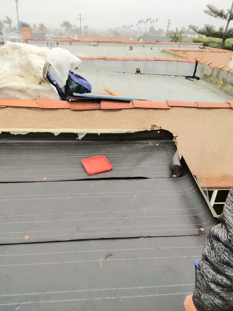 Base sheet being installed on a low-slope roof beside a stucco parapet with tile coping, on an attached ADU in Los Angeles